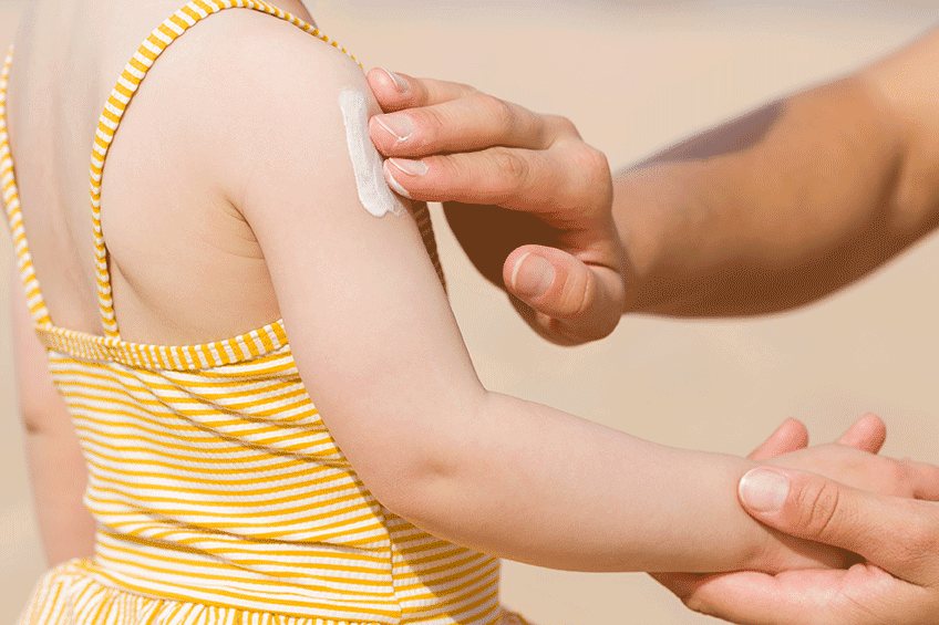 Photograph of a father's hand applying sunscreen to his child's arm