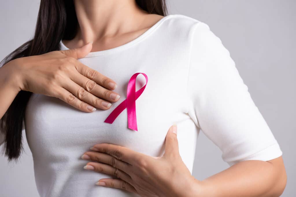 Woman in a white blouse with a pink ribbon on her chest, supporting the cause of breast cancer awareness