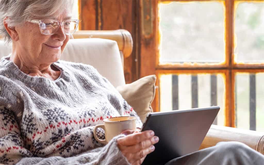 Happy senior woman drinking hot drink and using a tablet

