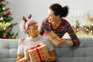 a woman giving a gift to a woman sitting on a couch